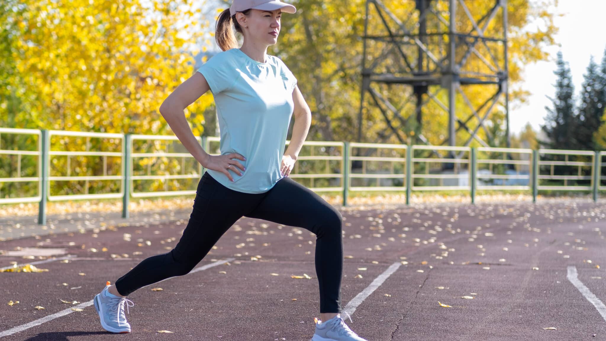 a young woman wearing ball cap warming up with walking lunges before a run. 