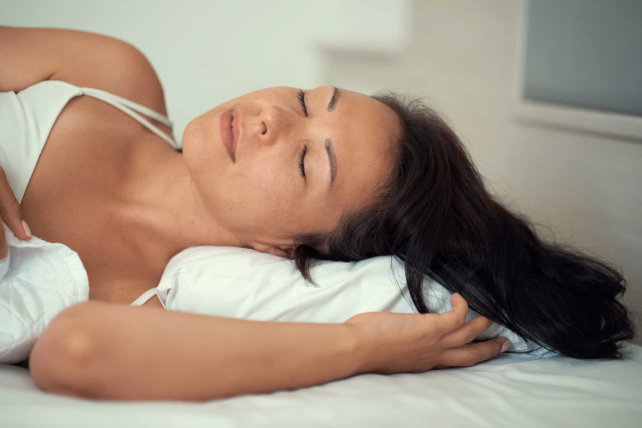 image of young smiling pretty lady lies in bed indoors. eyes closed.