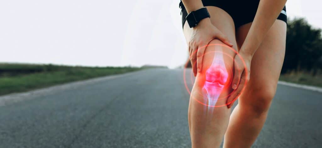 women running on parent stops to grasp her painful runner's knee, patellofemoral pain. 