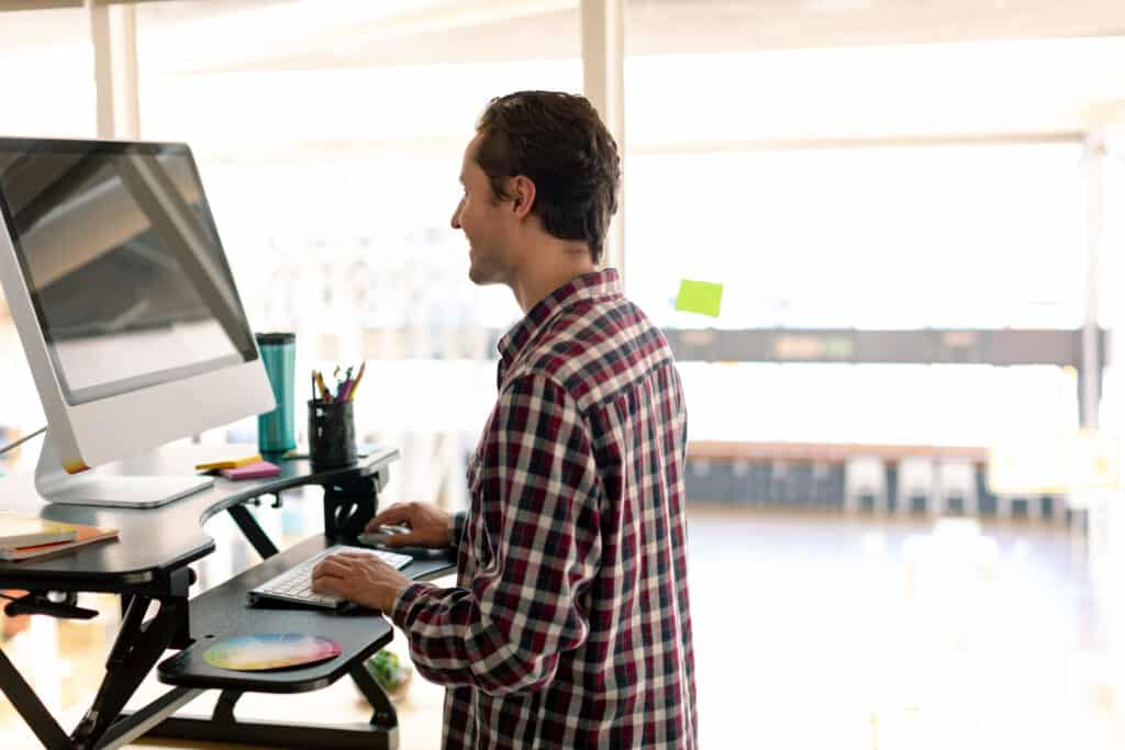 Caucasian male standing at a standing work desk working on a computer to avoid back pain when sitting.